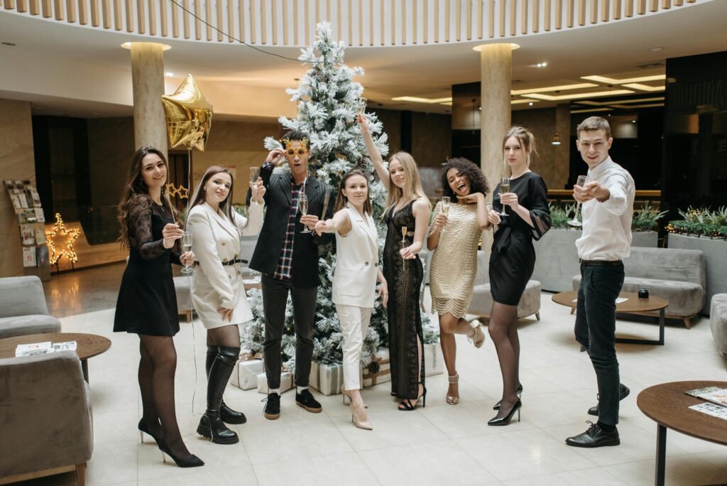 Group of stylish adults celebrating indoors next to a Christmas tree with drinks.